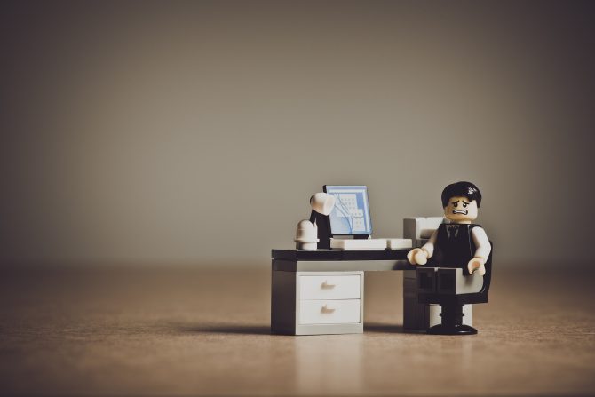 Lego čovječuljak koji sjedi na stolu u uredu s kompjuterom i lampom